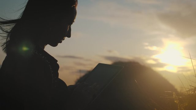 Girl farmer uses tablet in the field next to haystack at sunset. Smart farming, using modern technologies in agriculture.