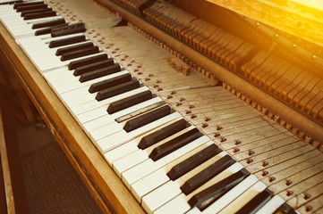 Angled view of old piano with broken keys and dust in warm lighting