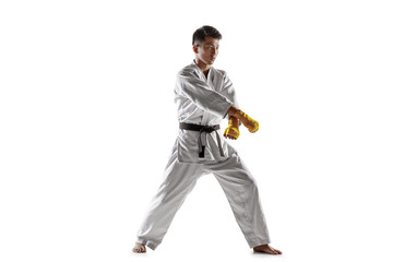 Naklejka premium Confident korean man in kimono practicing hand-to-hand combat, martial arts. Young male fighter with black belt training isolated on white studio background. Concept of healthy lifestyle, sport.