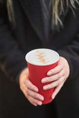 A young girl holds a cup with coffee in her hands. 