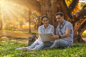 two young business people working with laptop computer together in park in autumn season