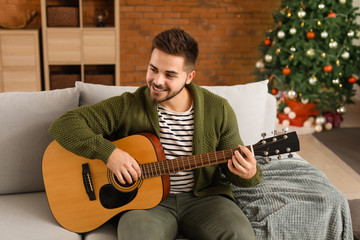 Handsome young man playing guitar at home on Christmas eve