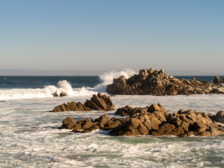 Waves crashing onto jagged rocks on the California coast near Monterey Bay.