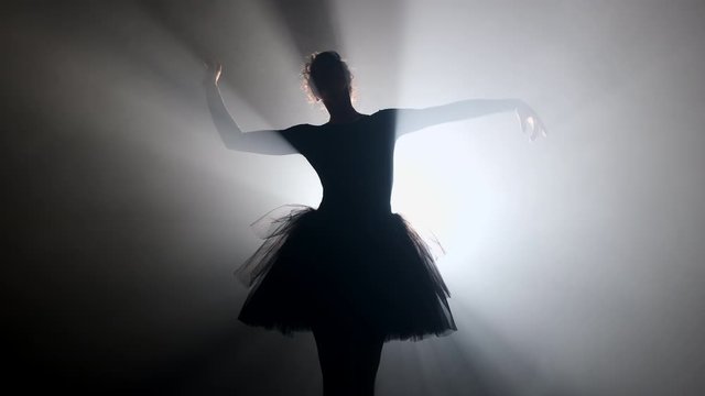 Professional ballerina dancing ballet in spotlights smoke on big stage.