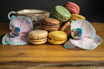 Colorful macarons, orchid flowers and a cup of tea put on wood table. Colorful macarons french dessert
