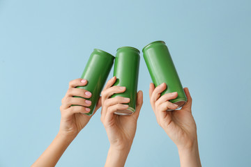 Hands with cans of beer on color background