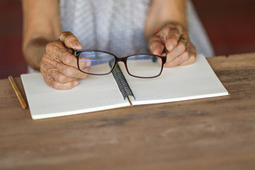 Old woman hands holding eye glasses on wooden table and notebook