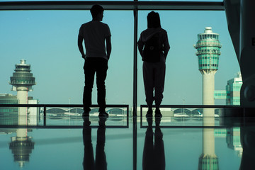 Silhouette back portrait of sweet couple stand inside the terminal and look out the runway and hanger at the airport