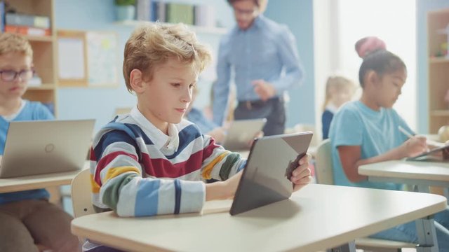 Elementary School Computer Science Class: Cute  Boy Uses Digital Tablet Computer, His Classmates work with Laptops too. Children Getting Modern Education in STEM, Playing and Learning - Powered by Adobe