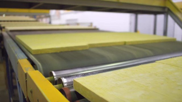 Close-up shot of finished slabs of rockwool moving over metal rollers onto conveyor belt at automated manufacturing facility