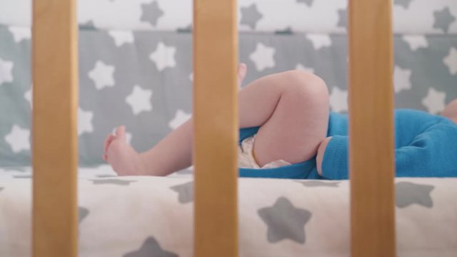 funny small baby kicks bare legs lying in new comfortable cot with stylish textile in children room