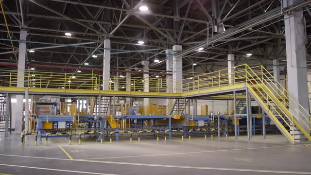 Wide arc shot of cavernous production hall, conveyor belt system, observation bridges and stairs at mineral wool manufacturing plant before start of shift