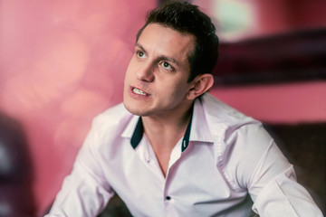 A young hispanic caucasian adult with a thinking expression against an abstract pink background wall. 