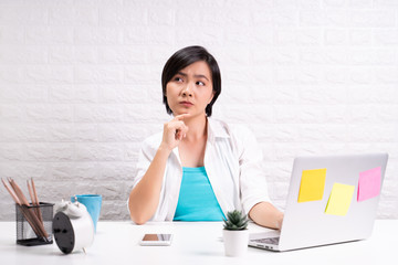 Thoughtful woman sitting at home office working using computer laptop