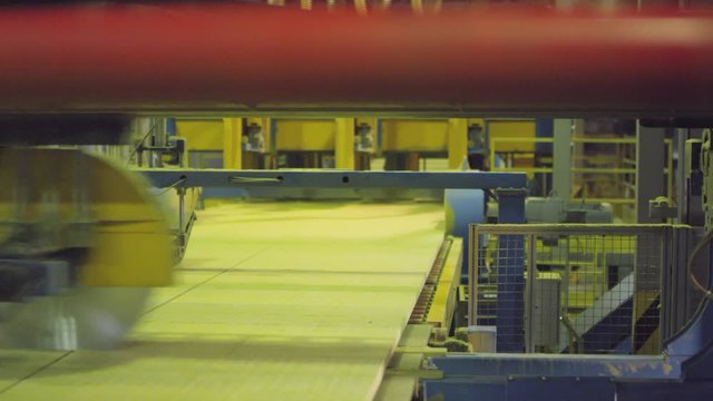 Close-up shot of industrial machine with large metal cutter wheel moving horizontally across finished hardened rockwool on production line and cutting it into even slabs