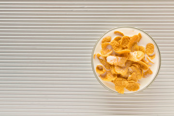 Cornflakes with milk in a plate on a silver background. The view from the top.