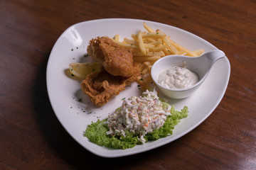 Fish and chips with coleslaw salad, tartar sauce on white plate, isolated over wooden background.