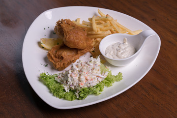 Fish and chips with coleslaw salad, tartar sauce on white plate, isolated over wooden background.