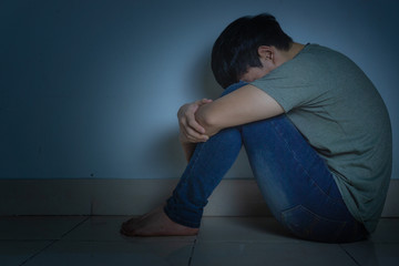 sad man hug his knee and cry sitting alone in a dark room. Depression, unhappy, stressed and...