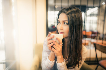 Beautiful Asian woman holding cup of coffee relaxing and drinking coffee in the corner of cafe