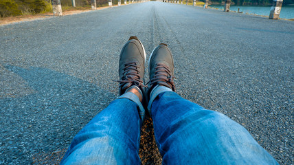 Human legs that wear jeans and lay down on the road 