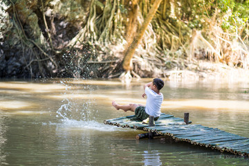 Kid boy sit on the Bamboo bridge beside the lake