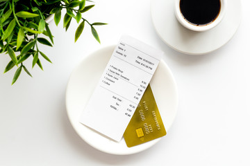 Paying in restaurant. Bank card near cup of coffee on white table top view
