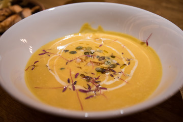 Life style, pumpkin soup on a white plate. Decorated with small plants. In the soft, muted light.
