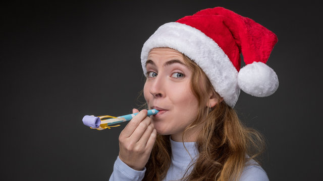 A beautiful woman in a red christmas hat blows on a party noise maker
