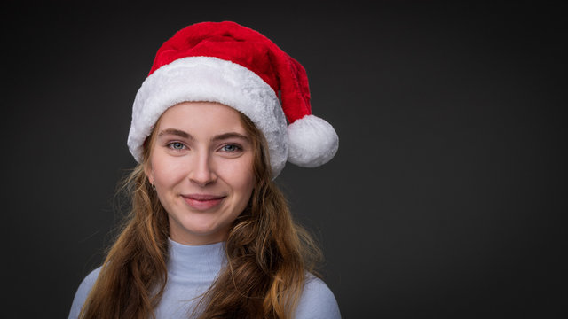 A georgous smiling woman wears a red Santa Claus hat and a blue turtle neck shirt