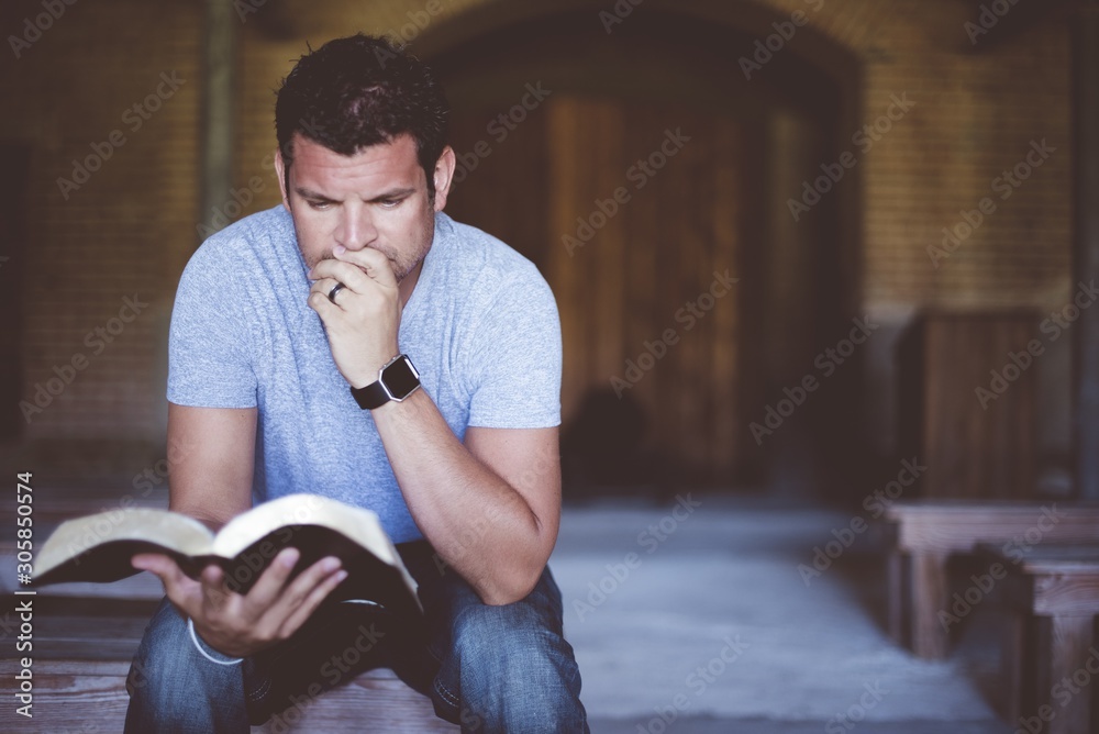 Wall mural closeup shot of a male sitting while reading the bible with a blurred background