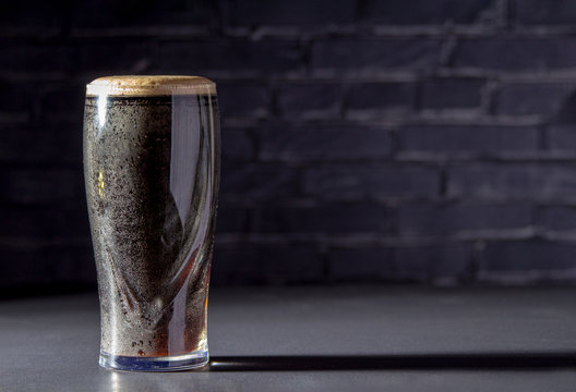 A dark Irish dry stout beer glass with a black brick on the background