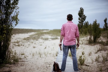 Male standing on the wooden pathway ear his bag while holding the bible with a blurred background