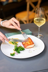 Lunch in a restaurant, a woman cuts the Salmon steak fillet and garnished with young broccoli. Restaurant menu, a series of photos of different dishes