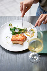 Lunch in a restaurant, a woman cuts the Salmon steak fillet and garnished with young broccoli. Restaurant menu, a series of photos of different dishes