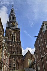 Fototapeta na wymiar Amsterdam, Holland. August 2019. The bell tower of the old church stands out in height on the houses making itself noticed from afar.