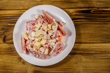 Tasty salad with crab sticks, cheese, tomato and mayonnaise on wooden table. Top view