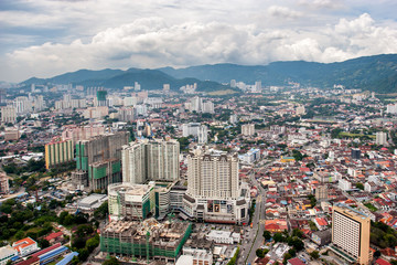 View from a skyscraper at Georgetown city on Penang island in Malaysia. Lots of tall buildings and small houses. Mountains on the horizon.