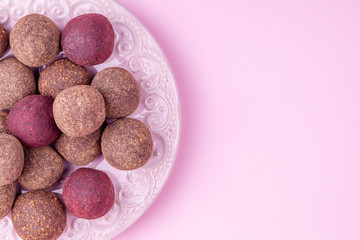 Homemade Raw Vegan Cacao Energy Balls on Plate on Pink Background. Healthy Chocolate Candy from Nuts, Dates and Peanuts. Concept of Natural Vegetarian Handmade Dessert. Top View. Copy Space