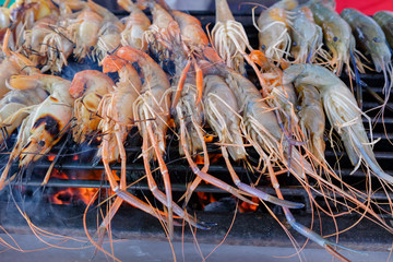 Grilled shrimps on the flaming grill with flames in background in Thailand market