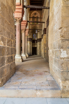 Passage at Sultan Qalawun Mosque with stone columns, colored stained glass windows and wooden door, Cairo, Egypt