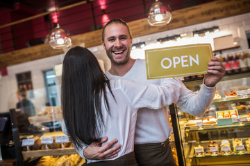 Dark-haired wife hugging husband after opening bakery together