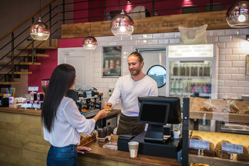 Dark-haired woman paying for her order in coffee shop by card