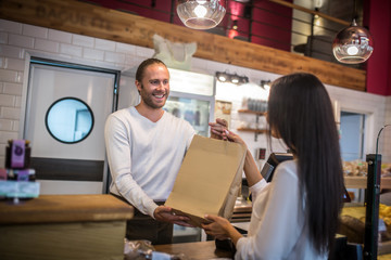 Smiling barista passing the bag with takeaway coffee to the customer
