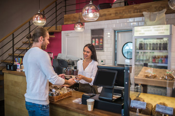 Smiling cashier passing takeaway coffees to her constant customer