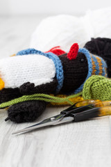 Knitted parts for woolen penguin toy with scissors and knitting needles.  On a grey wood surface.  Craft hobby concept