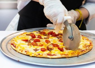 Slicing Fresh Made Italian Pizza, Closeup hand of chef cutting pizza in kitchen