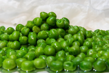 Close up of many stacked cooked English peas on white  background . Selective focus. Food concept of organic green peas  on  plate. Lunch, dinner vegetables, vegan food.