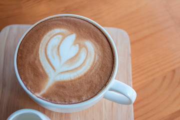Latte coffee cup with latte art on wooden table in coffee shop.