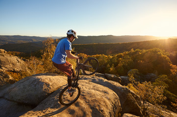 Fearless cyclist balancing on back wheel on trial bike. Sportsman biker making acrobatic stunt on...
